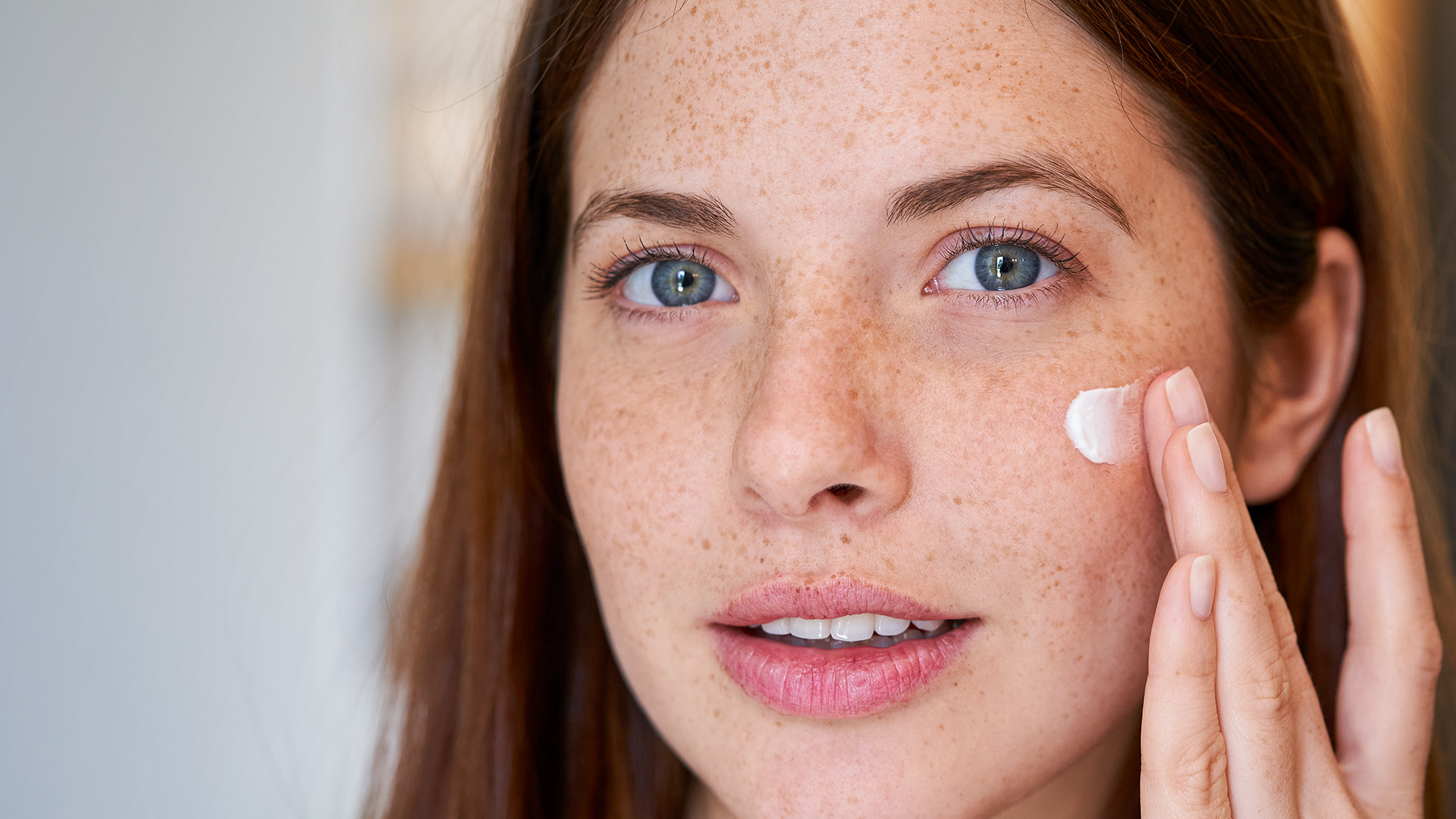 Junge Frau mit Sommersprossen trägt Gesichtscreme auf