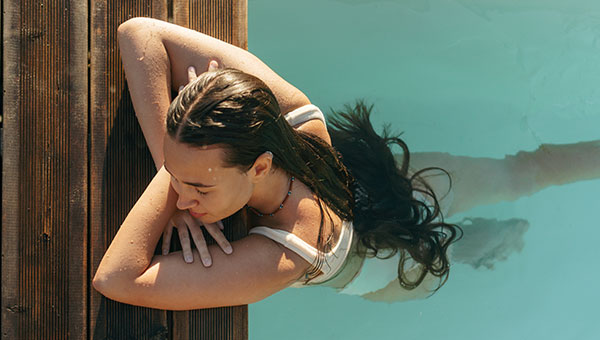 Frau im Pool, genießt das Wasser und die warme Sonne.