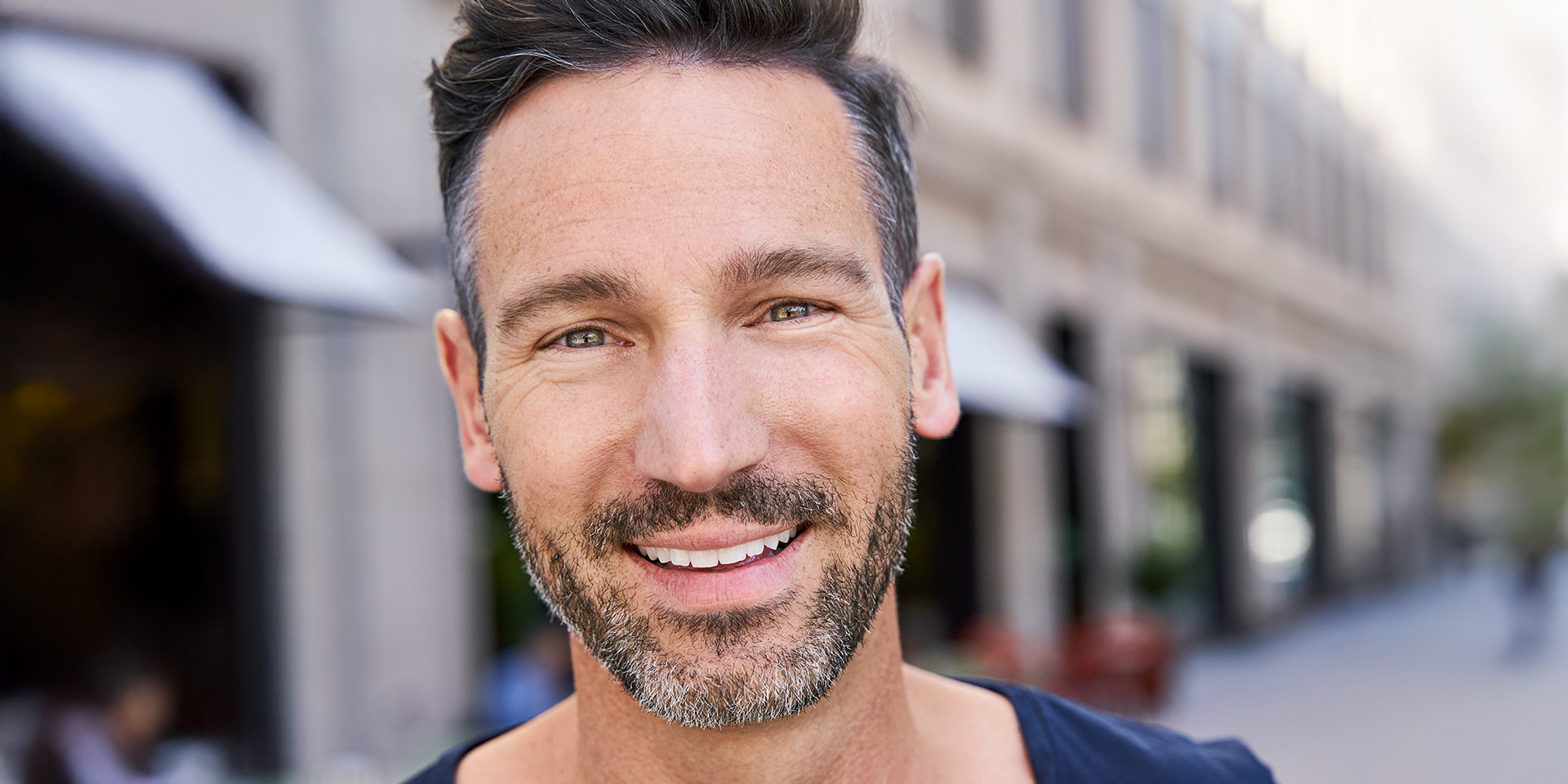 Mann in Stadt blickt lächelend in Kamera