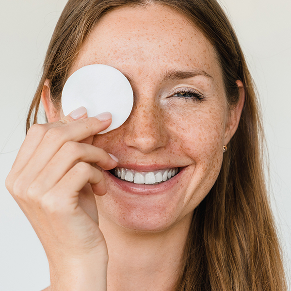 Lächelnde Frau reinigt sanft die Augenpartie mit einem Wattepad