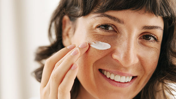 Close-Up von Frau die Creme aufträgt und in die Kamera lächelt